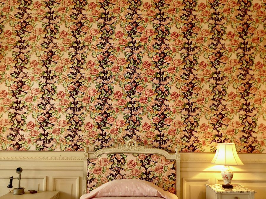 Bedroom with a richly patterned vintage floral wallpaper and a warm bedside table lamp