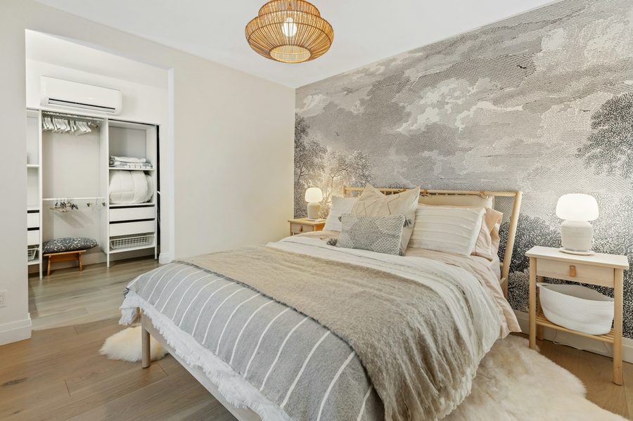 Bedroom with a soft grey landscape mural wallpaper behind a neutral, layered bed